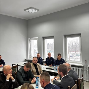 Trzech komendantów siedzą za biurkiem, a przed nimi siedzą przedstawiciele samorządów.