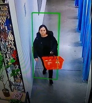 Kobieta ubrana na czarno z czerwonym koszykiem w ręku.