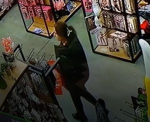 Kobieta ubrana na czarno z czerwonym koszykiem w ręku między regałami.