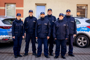 Sześciu dzielnicowych na tle radiowozów.