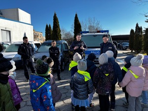 Policjanci stoją przed dziećmi na zewnątrz.