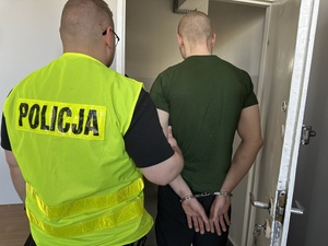 Policjant prowadzi mężczyznę w kajdankach.