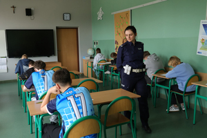 Policjantka przechodzi obok dzieci piszących test w ławkach.