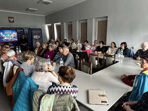 Seniorzy siedzą w auli Komendy Powiatowej Policji w Bełchatowie.