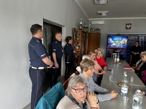 Policjanci stoją przed seniorami w auli Komendy Powiatowej Policji w Bełchatowie.