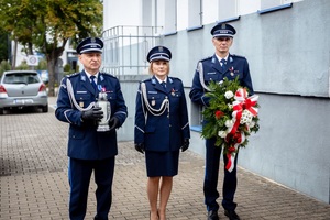 Oficerowie składają kwiaty i znicz przed tablicą pamiątkową.