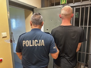 Mężczyzna tyłem trzymany przez policjanta.