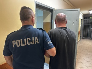 Mężczyzna tyłem trzymany przez policjanta.