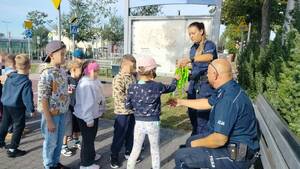 Policjanci rozdają gadżety odblaskowe dzieciom.