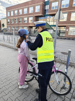 Policjant zakłada kask dziewczynce na głowę.