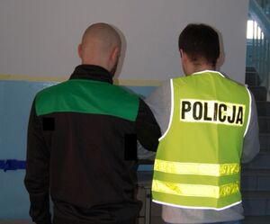 zatrzymany mężczyzna przy nim stoi policjant, zdjęcie zrobione w pomieszczeniu służbowym.