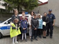 uczniowie ze Szkoły Podstawowej w Szczercowie na spotkaniu z policjantami. Zdjęcie pokazuje dzielnicowego z uczniami i ich opiekunami . Wszyscy stoją przy policyjnym radiowozie.