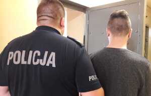 zatrzymany za posiadanie narkotyków, policjant wprowadza podejrzanego do pomieszczenia dla zatrzymanych