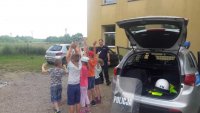 policjant na spotkaniu z uczniami, policjant pokazuje dzieciom radiowóz i policyjne akcesoria